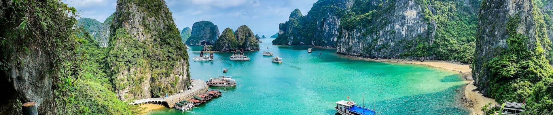 Panoramic view of Ha Long Bay, Vietnam with limestone karsts, turquoise water, and cruise boats under a clear blue sky.