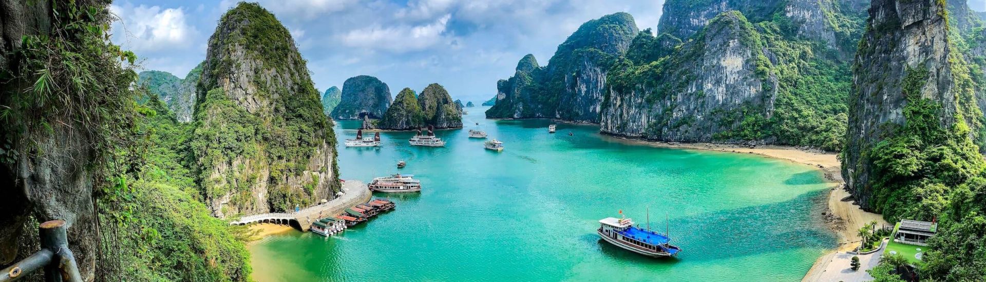Panoramic view of Ha Long Bay, Vietnam with limestone karsts, turquoise water, and cruise boats under a clear blue sky.