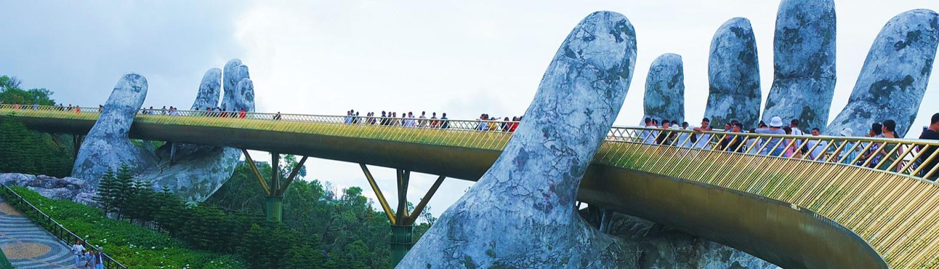 Tourists walking across the Golden Bridge at Ba Na Hills in Da Nang, Vietnam – a stunning pedestrian bridge held by giant stone hands surrounded by lush mountains.